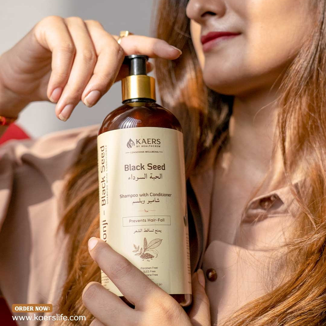 Woman holding a bottle of Kaers Black Seed hair care shampoo with a blurred background
