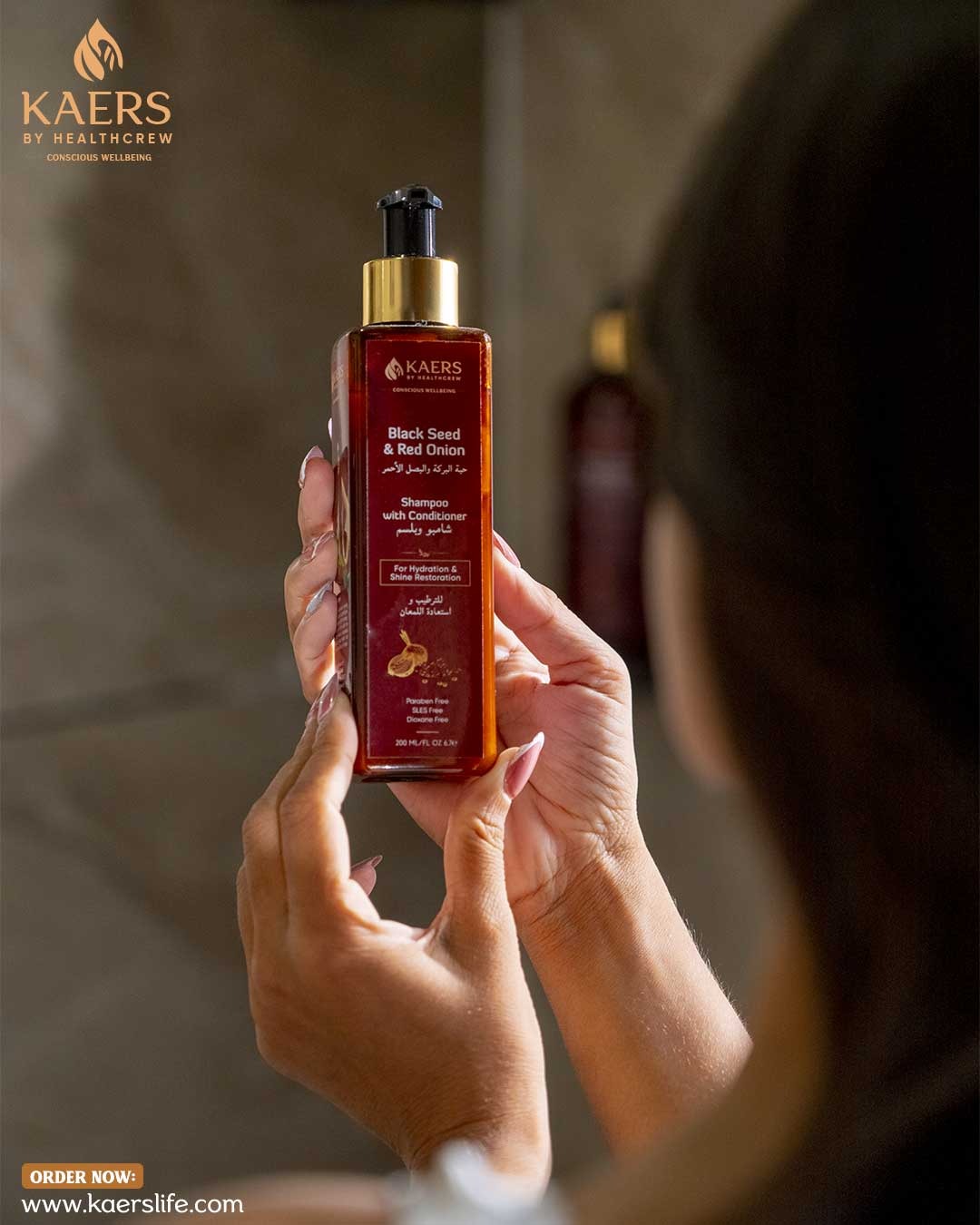 Person holding a KAERS hair care shampoo wih black seed and red onion product bottle with blurred background