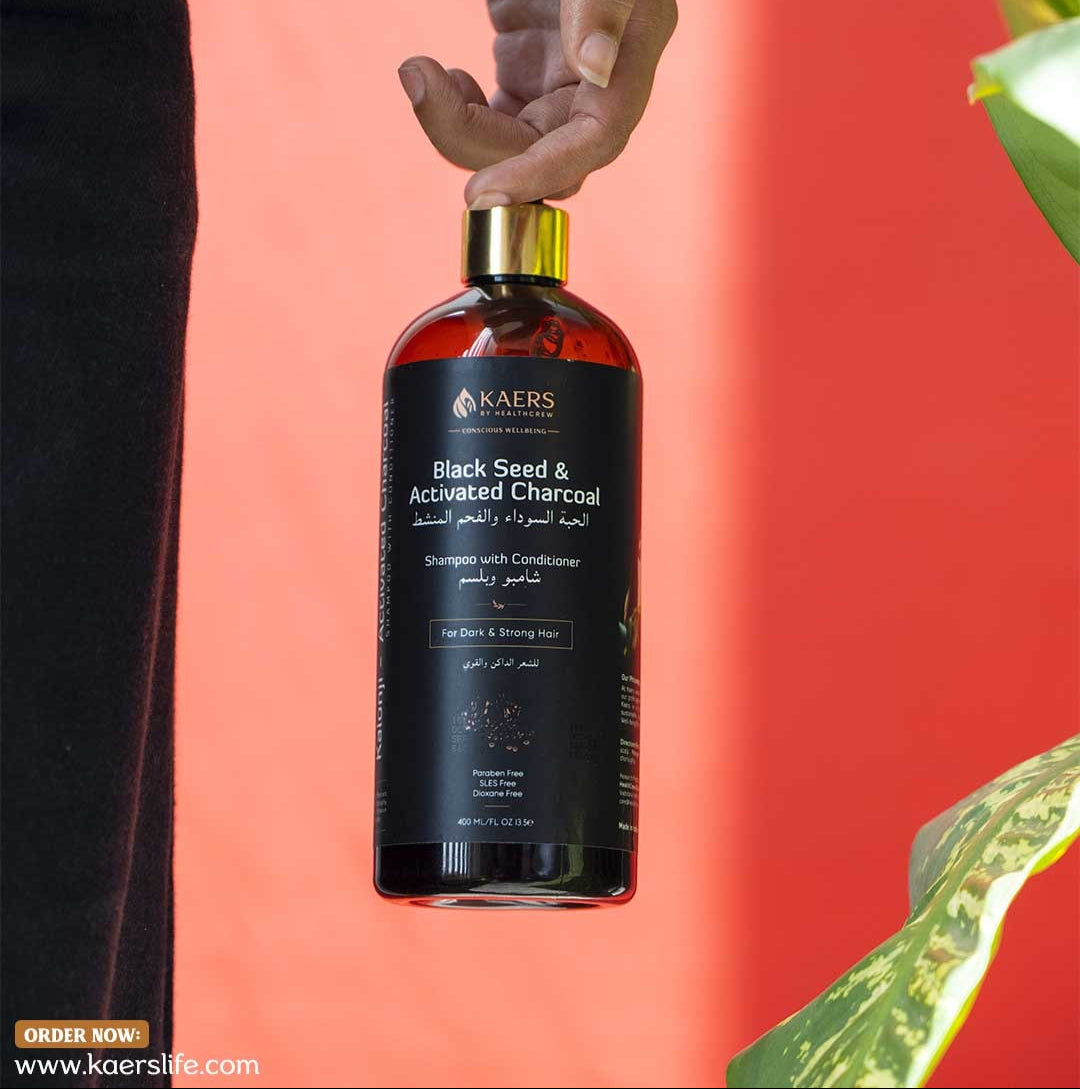 Bottle of Kaers Black Seed & Activated Charcoal shampoo with conditioner against a red background