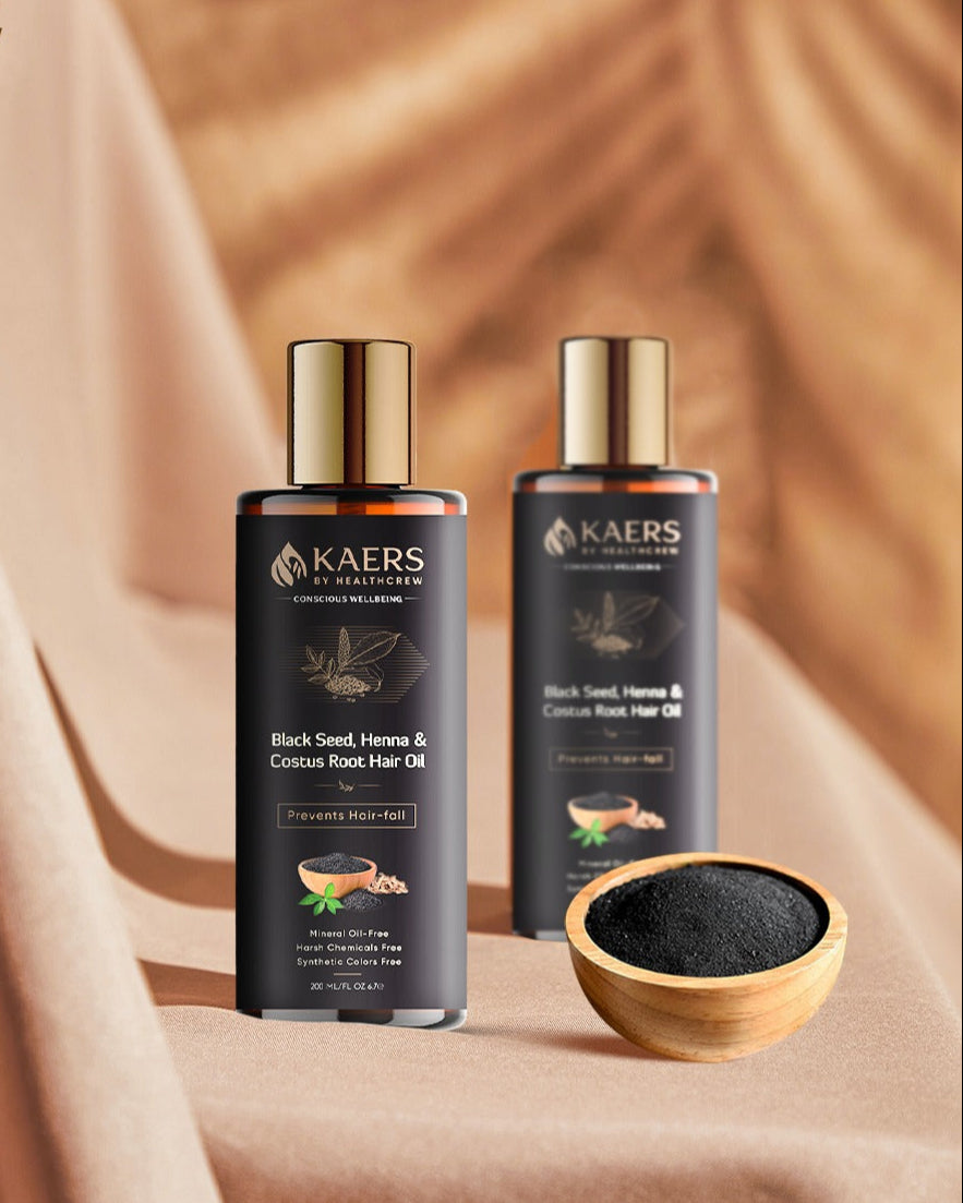 Two bottles of Kaers Black Seed, Henna & Coirnut Root Hair Oil on a beige background with a small bowl of kalonji.