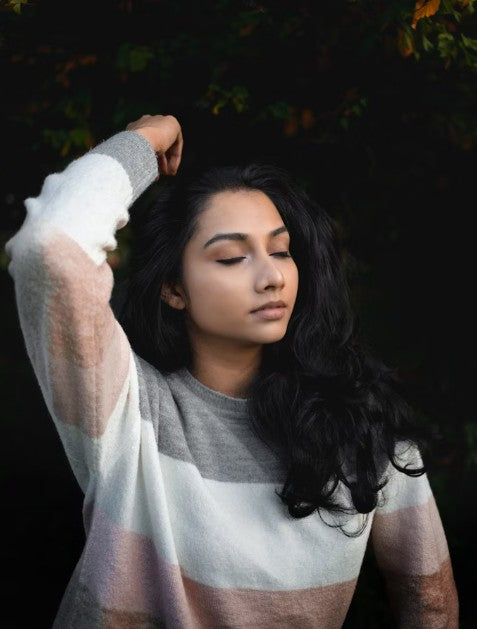 Kaers Woman with long dark hair wearing a striped sweater against a dark background