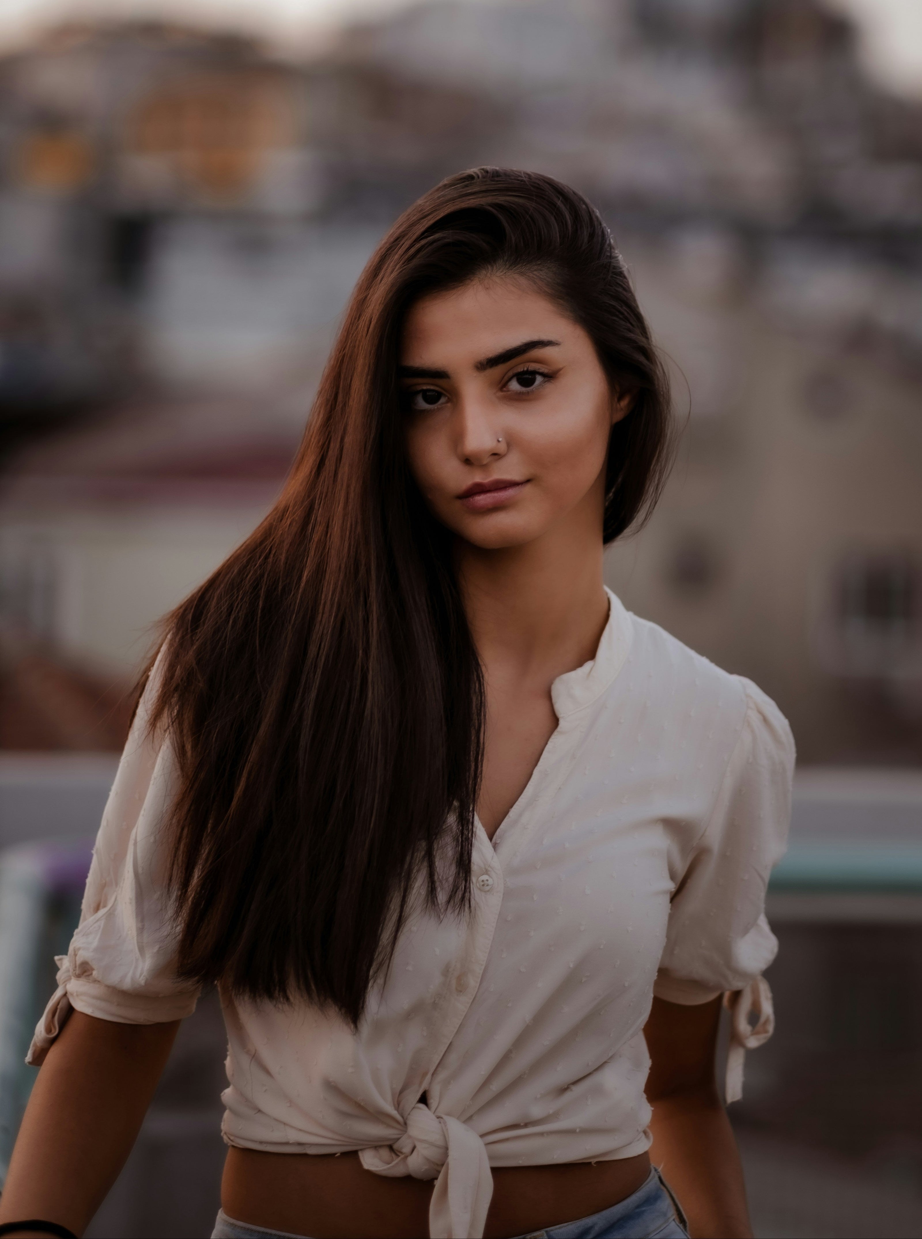 Kaers Woman in a white shirt standing in front of a blurred cityscape