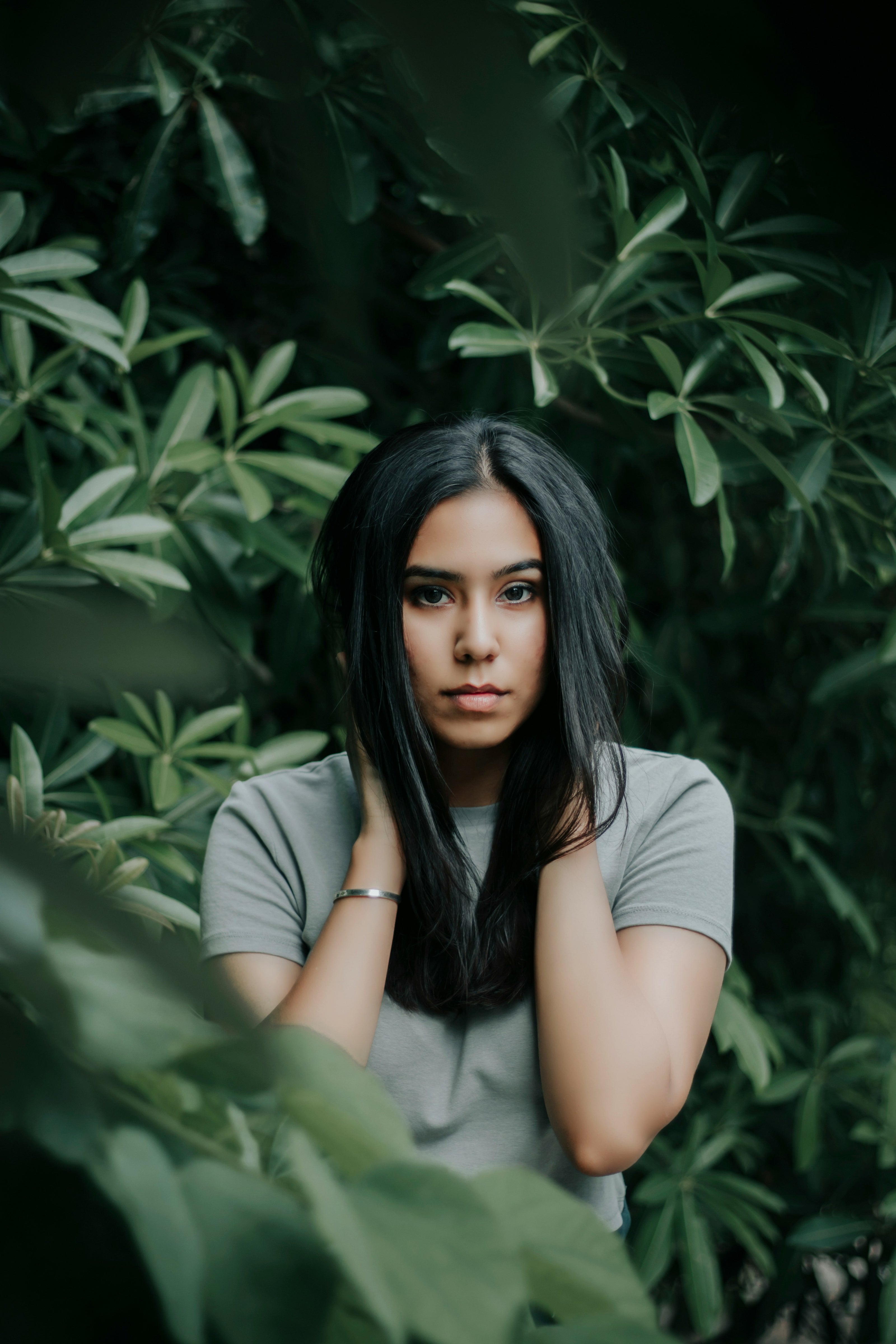 Kaers Woman with long dark hair sitting among green foliage