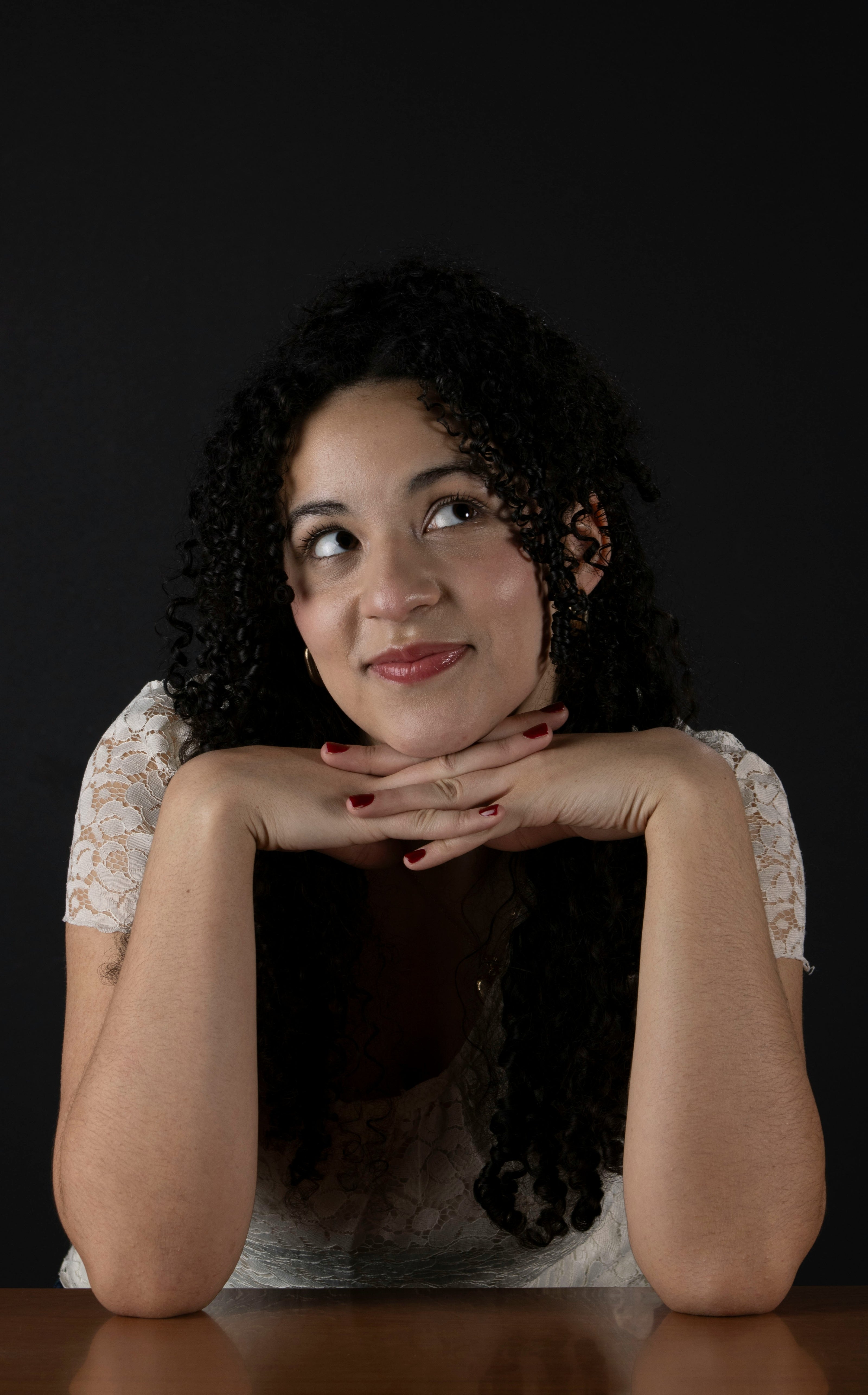 Kaers Woman with curly hair resting her chin on her hands against a black background
