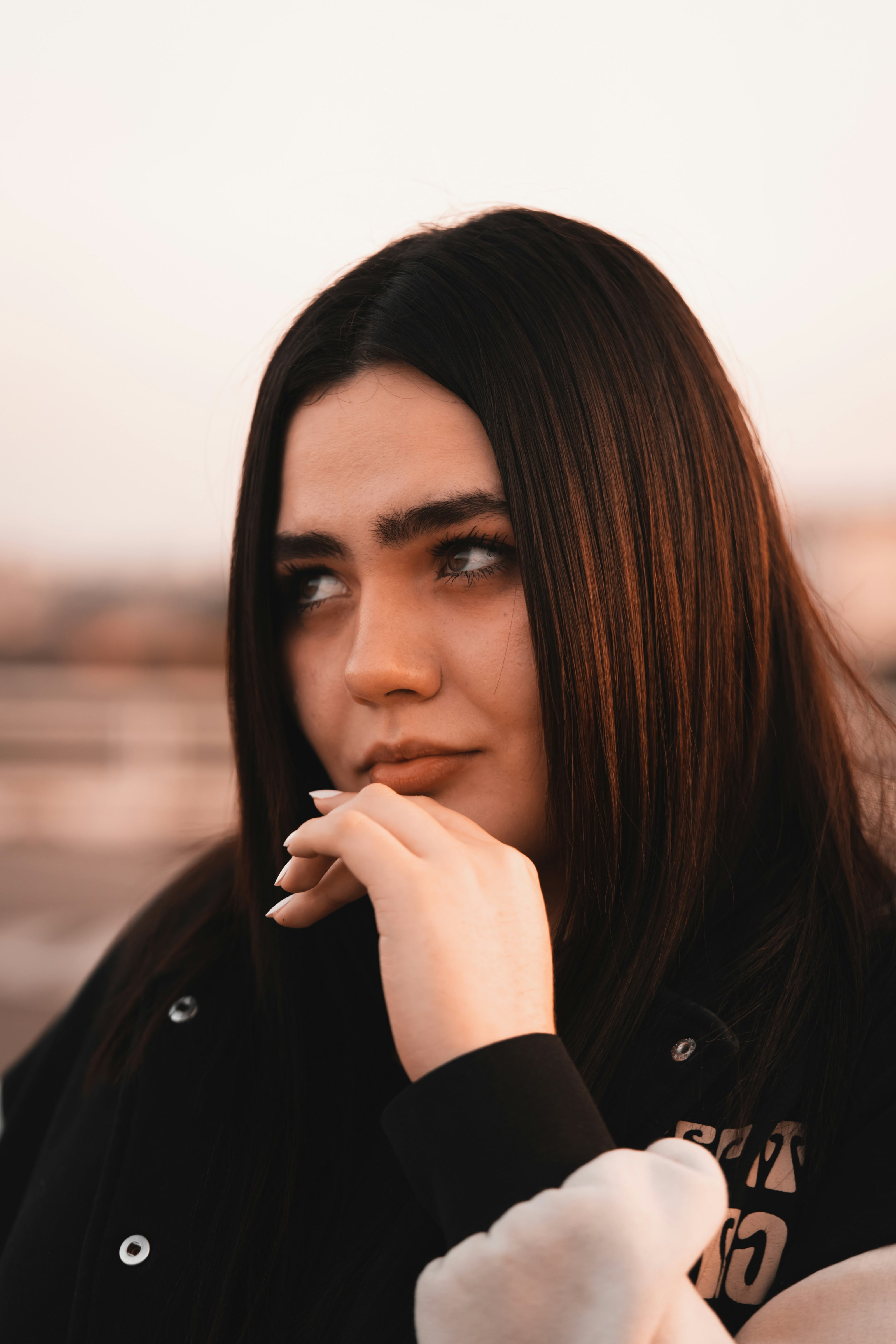 Woman with long dark hair by kaers shampoo wearing a black jacket with visible branding.