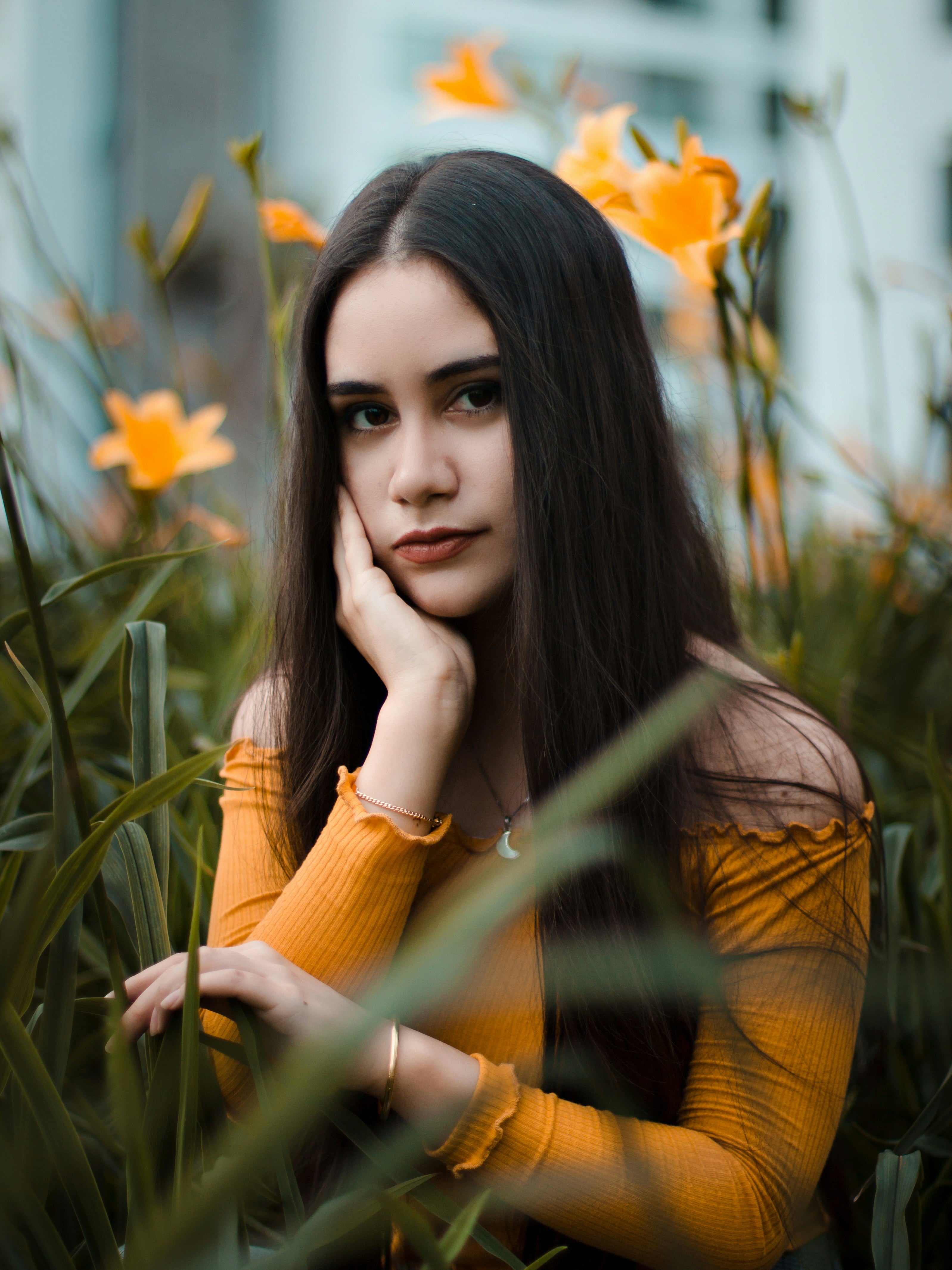 Woman in an orange top sitting among green plants and orange flowers