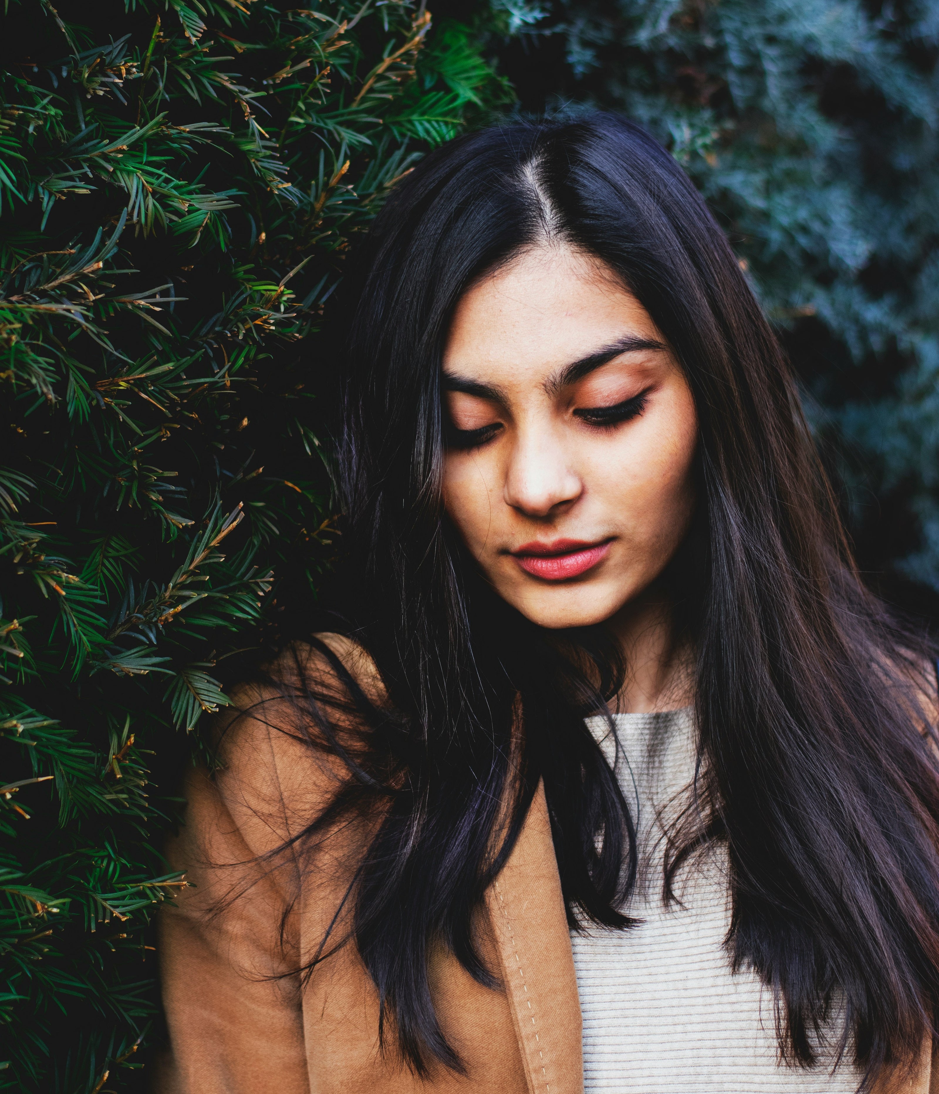 Kaers Woman with long dark hair standing against a green bush