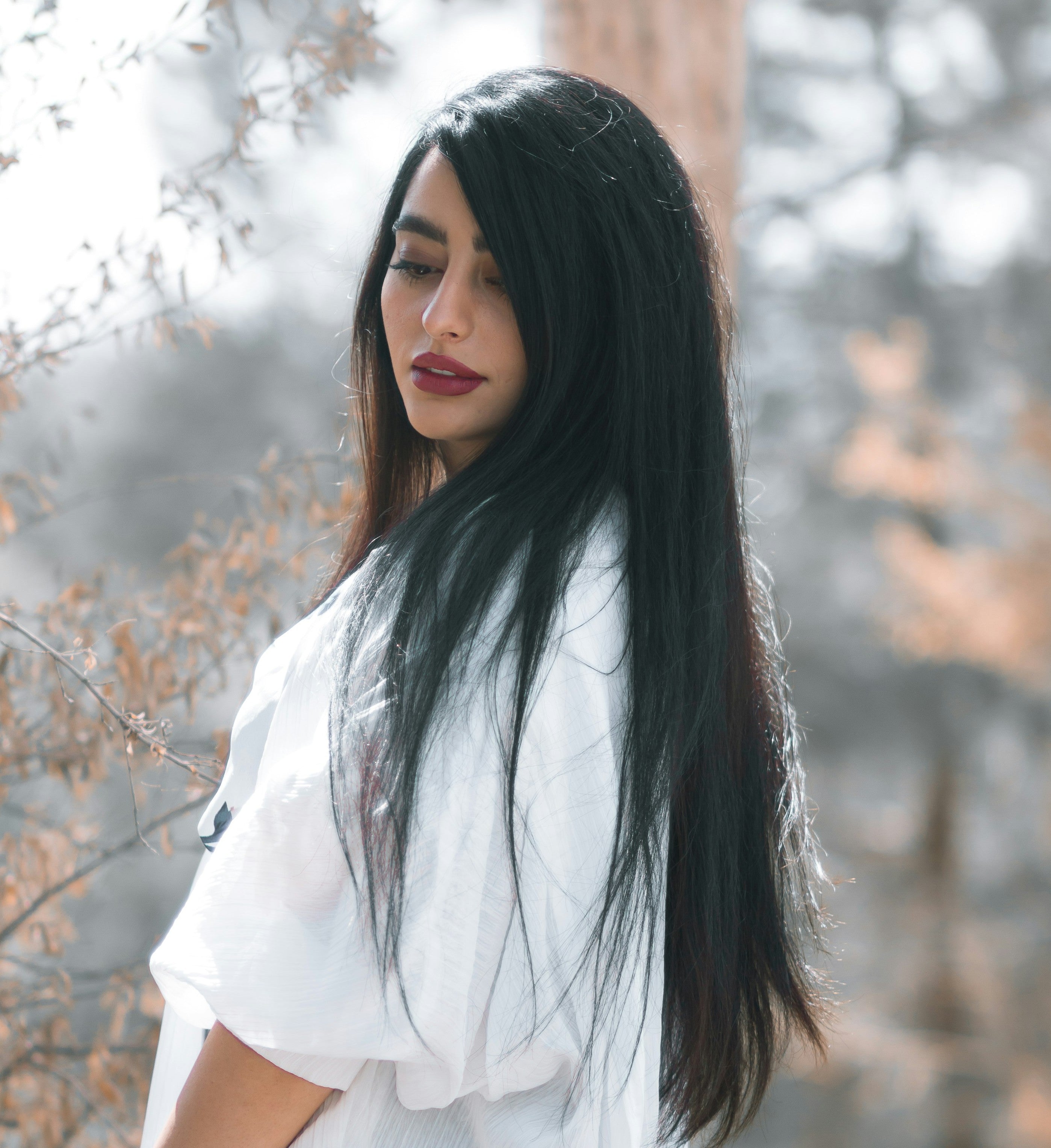 Kaers Woman with long black hair wearing a white top against a blurred natural background