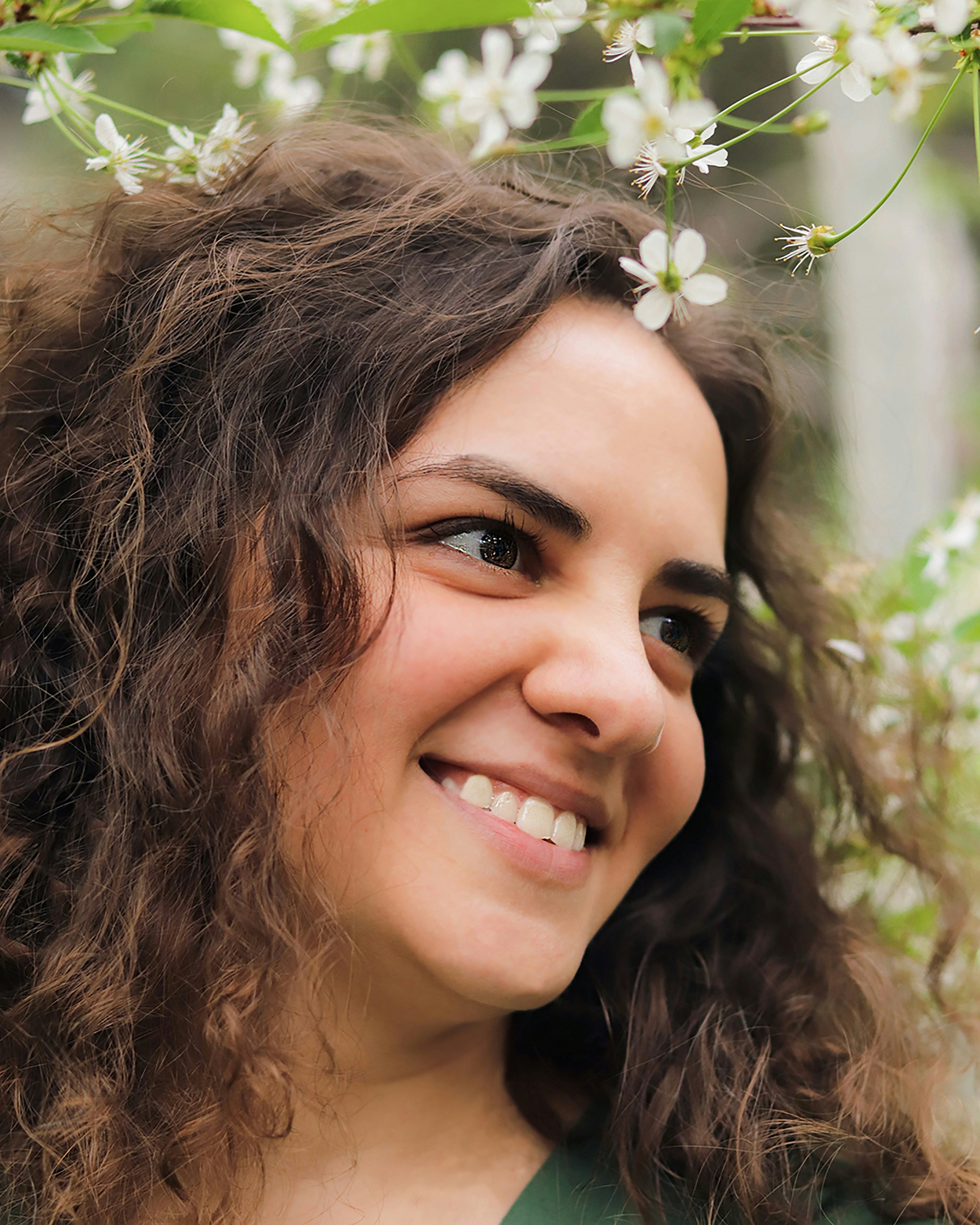 Kaers Woman with curly hair and a green top, surrounded by white flowers and greenery