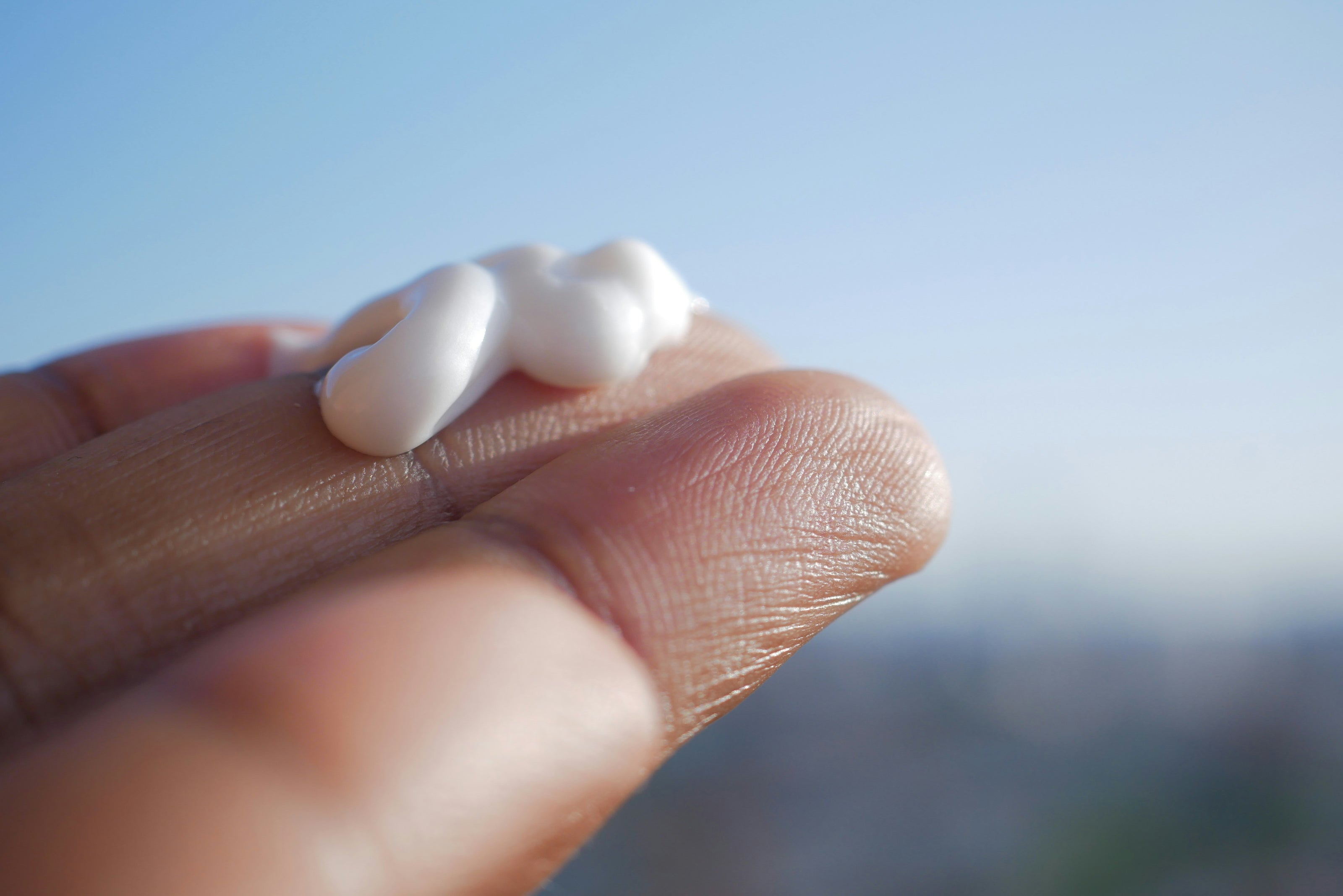 Hand holding a small amount of white cream against a blurred natural background - kaers whipped body butter